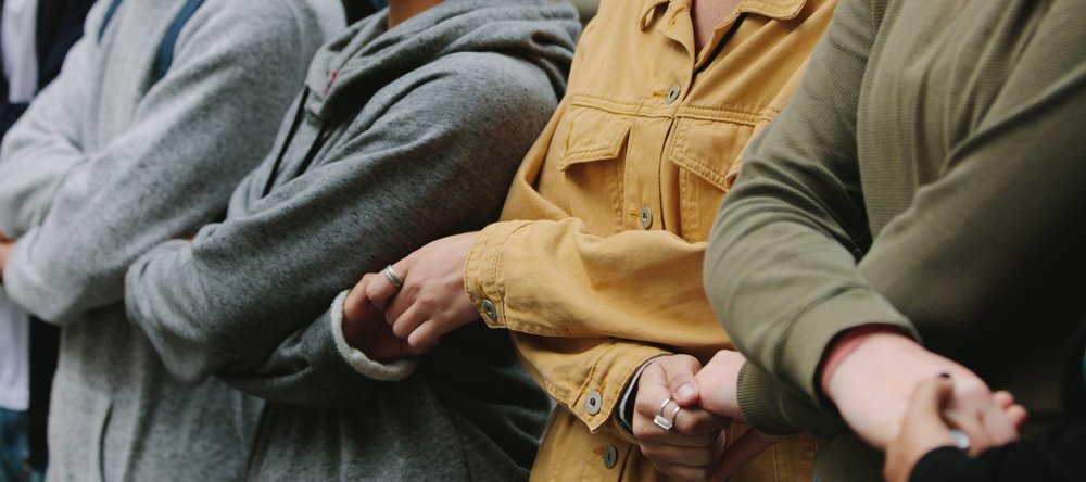 Zbliżenie na sylwetki 4 osób stojących w rzędzie i trzymających się za ręce